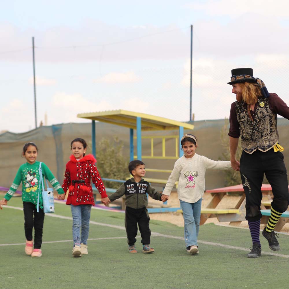 Children holding hands and smiling at the start of a Flying Seagull performance in one of Jordan's largest refugee camps.
